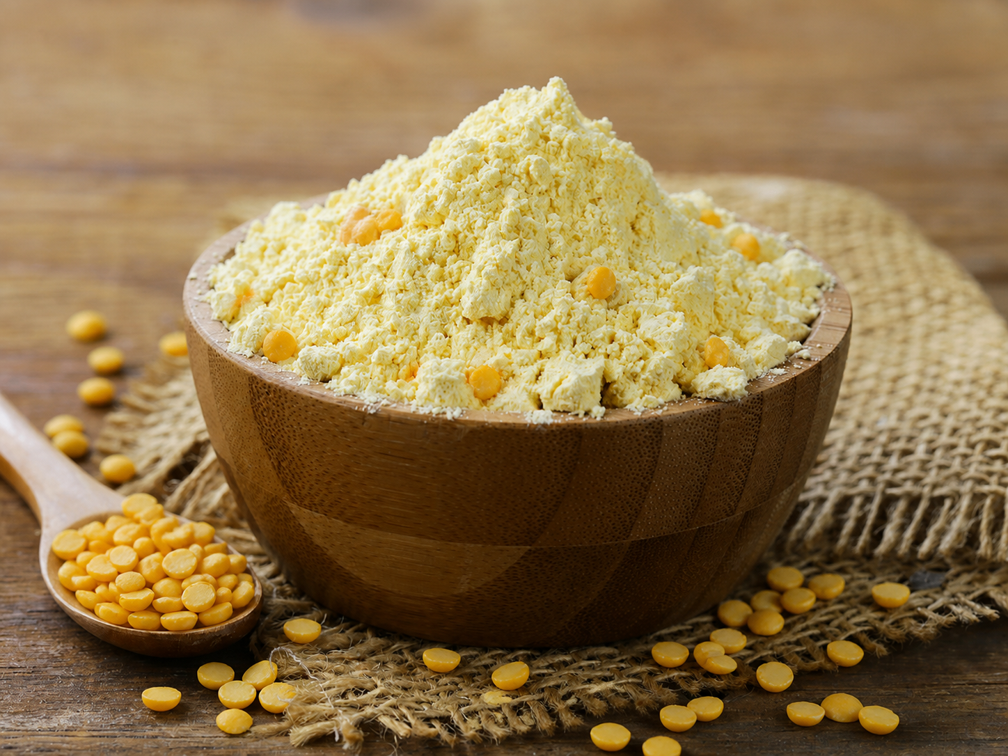 A wooden bowl of golden chana dal besan surrounded by yellow split chana dal